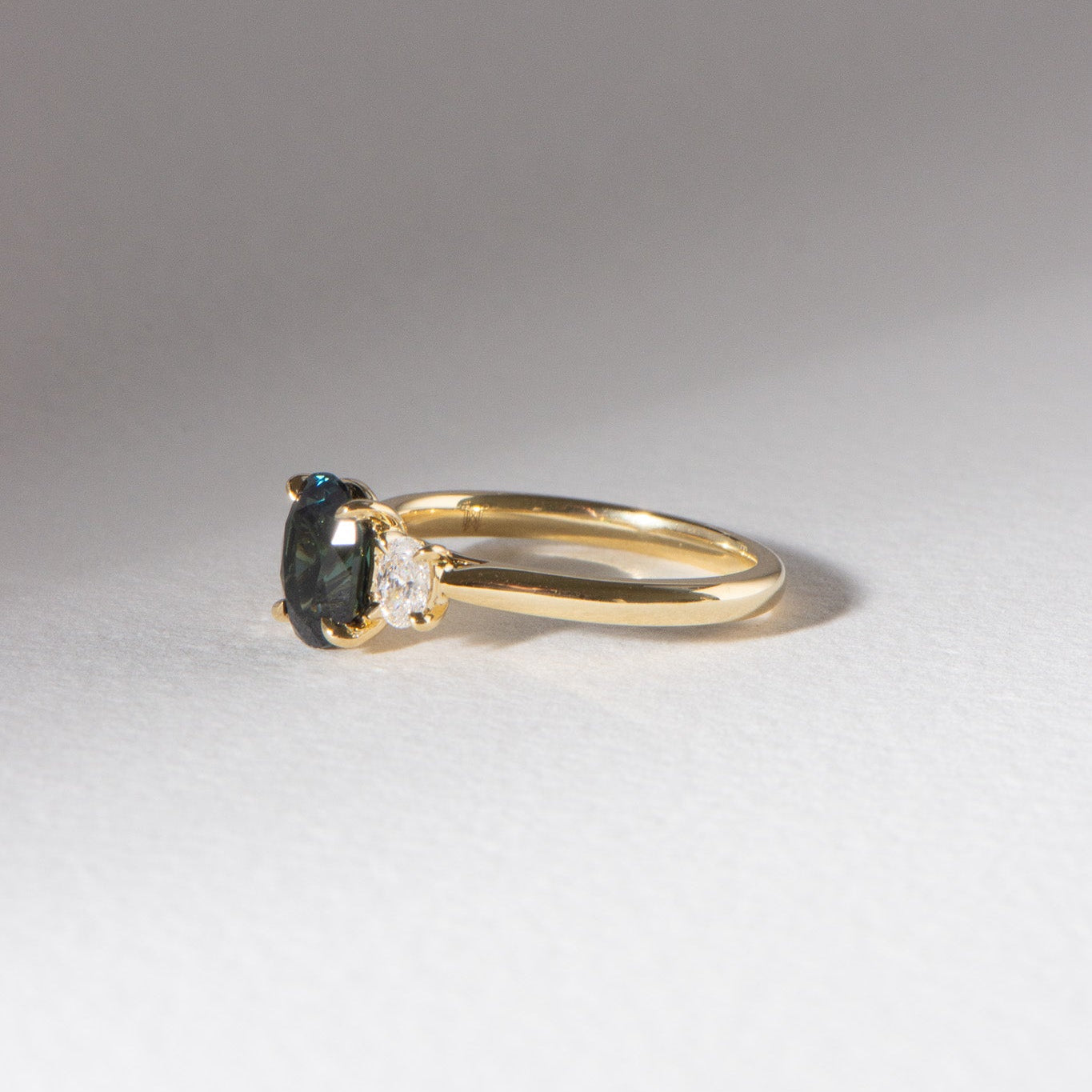 Australian blueish teal sapphire engagement ring with 1.78ct centre sapphire, 0.29ct oval lab diamonds, set in 18k yellow gold cathedral three-stone setting.