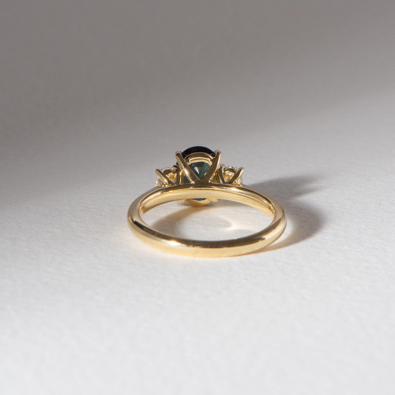 Australian blueish teal sapphire engagement ring with 1.78ct centre sapphire, 0.29ct oval lab diamonds, set in 18k yellow gold cathedral three-stone setting.